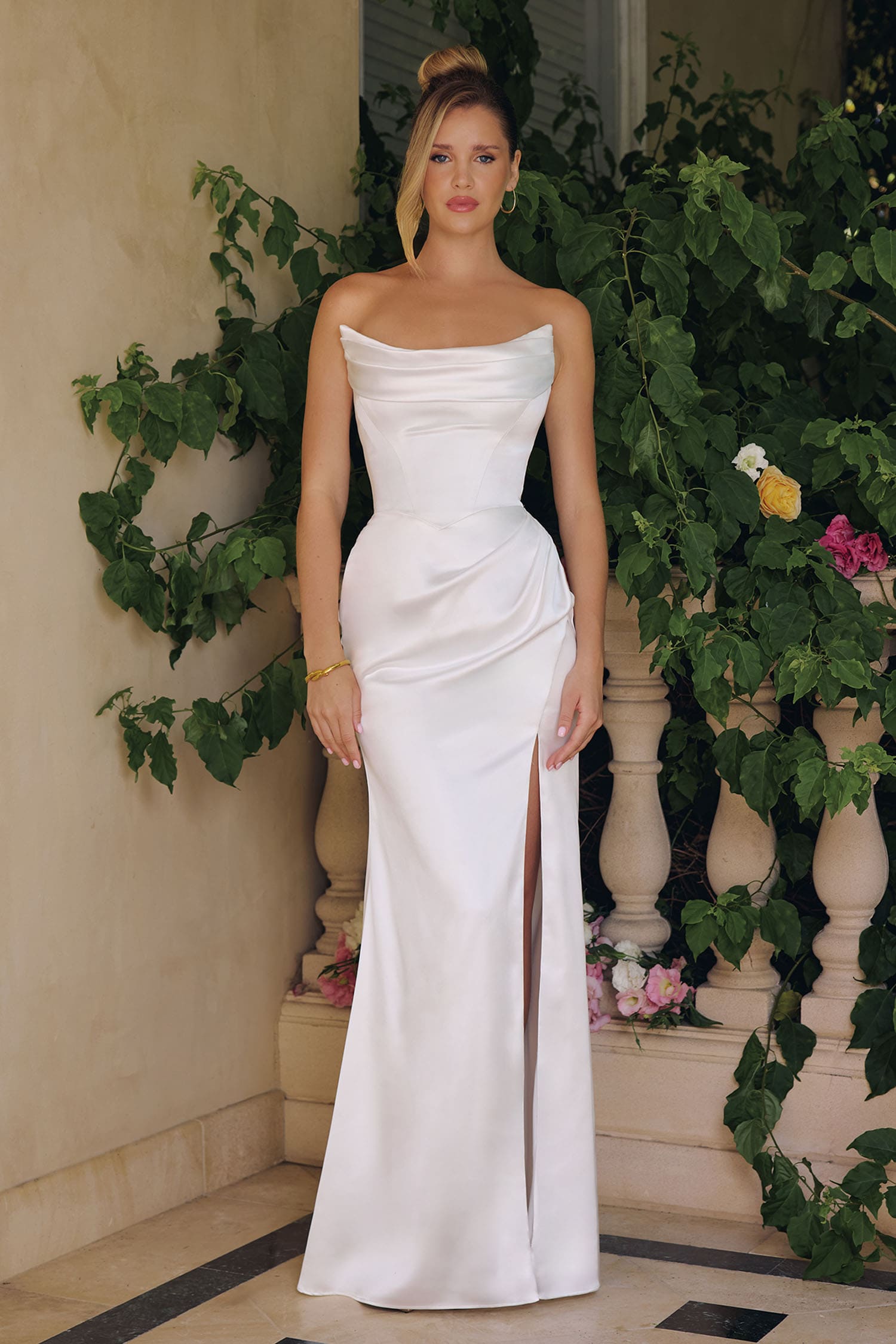 Woman in a white strapless gown standing in front of greenery