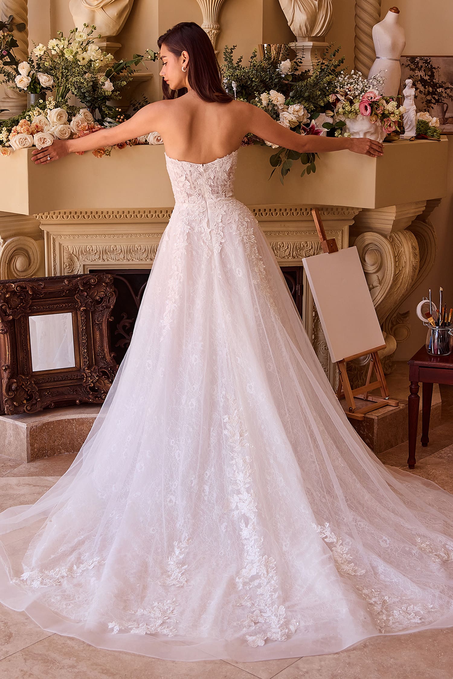 Woman in a white wedding dress standing in an elegant room with floral arrangements.