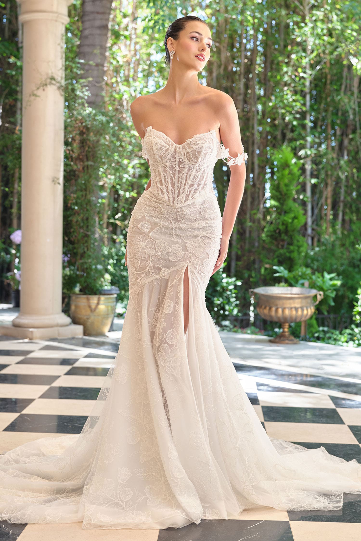 Woman in a white strapless gown standing in an outdoor setting with columns and greenery.