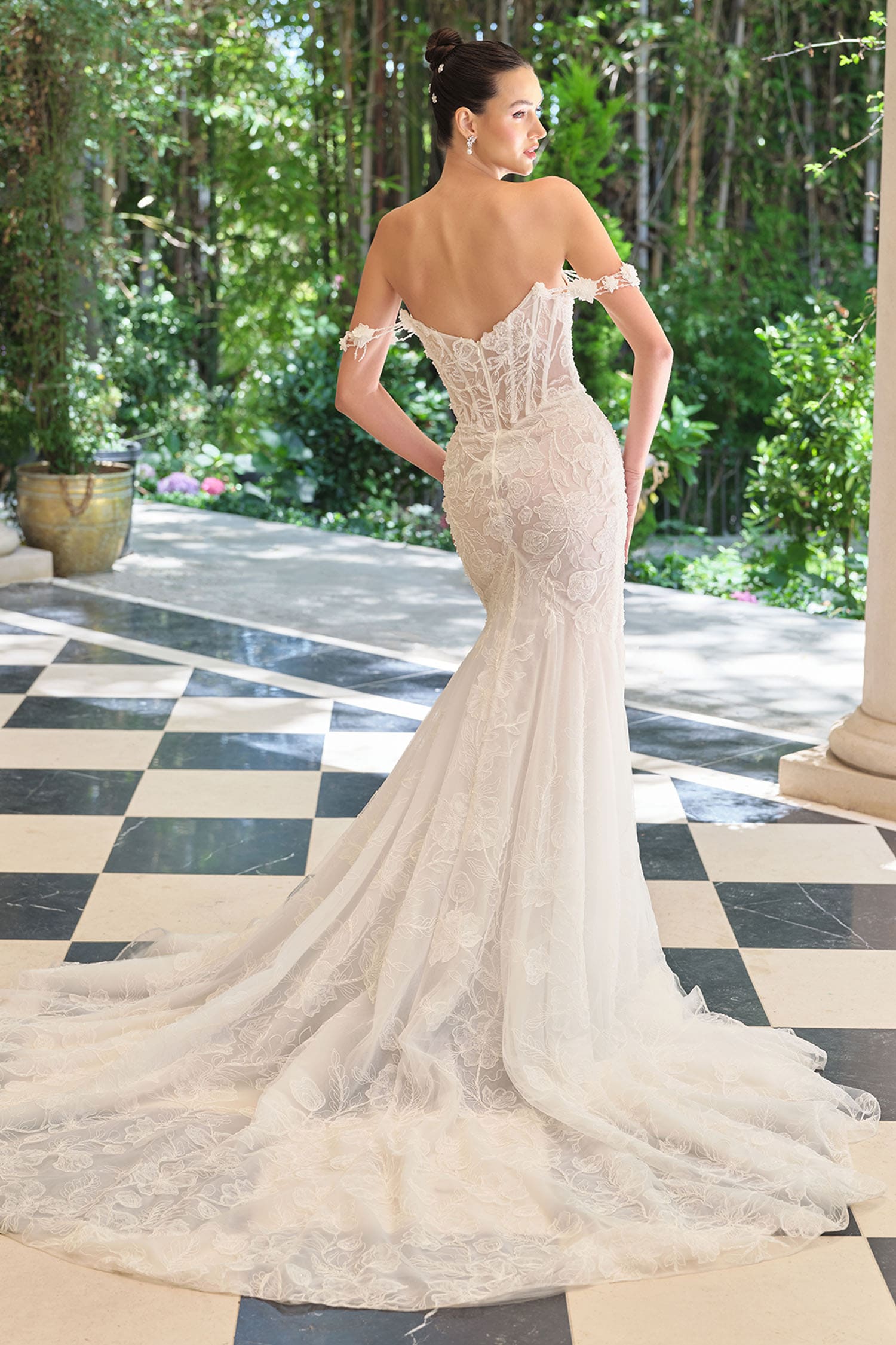 Woman in a white lace wedding dress standing on a checkered floor with greenery in the background