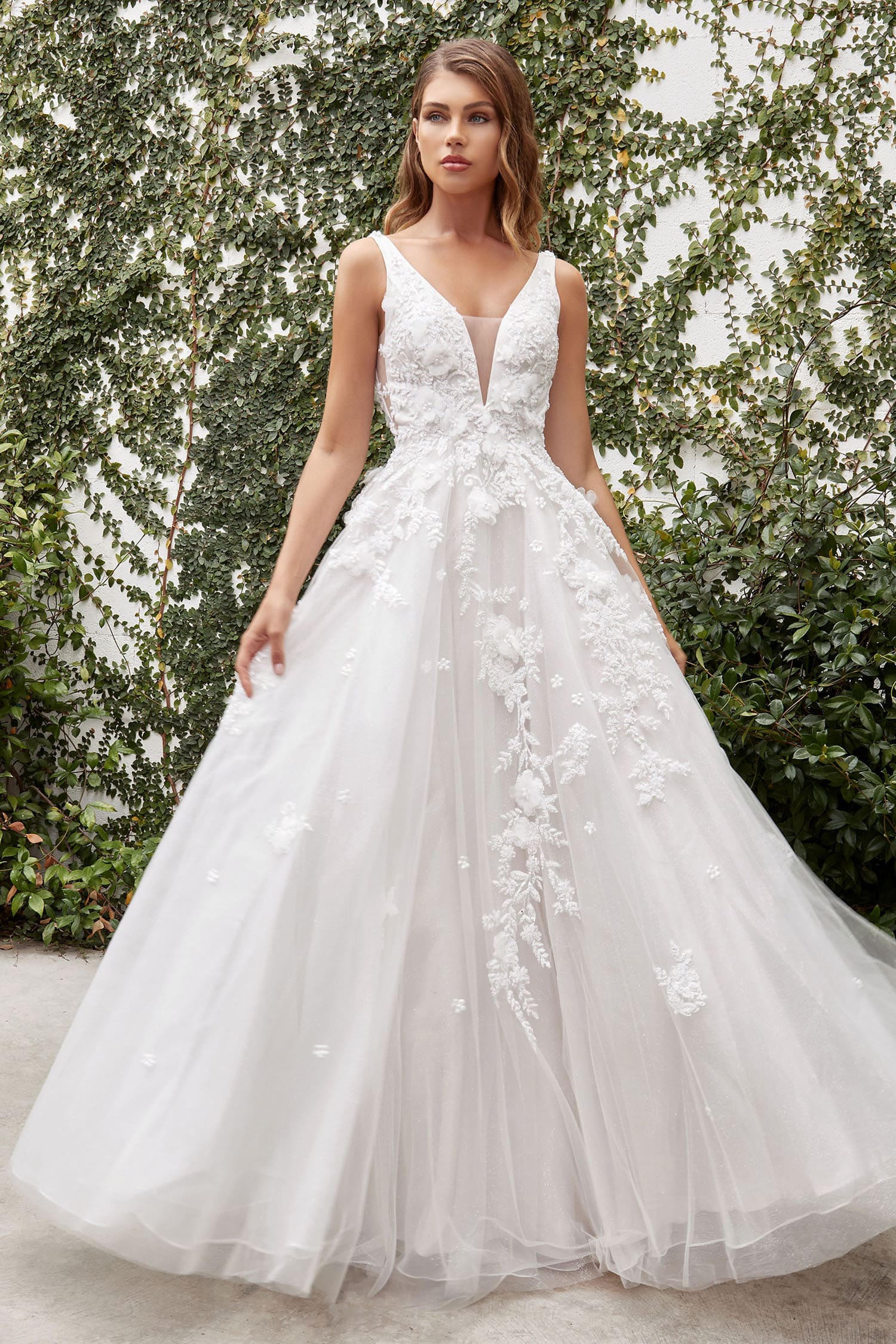 White wedding dress with floral details worn by a model against a green foliage background