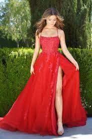 A person is wearing a vibrant red gown with a high slit, gracefully walking outdoors. The background features lush greenery, emphasizing the elegance of the attire.