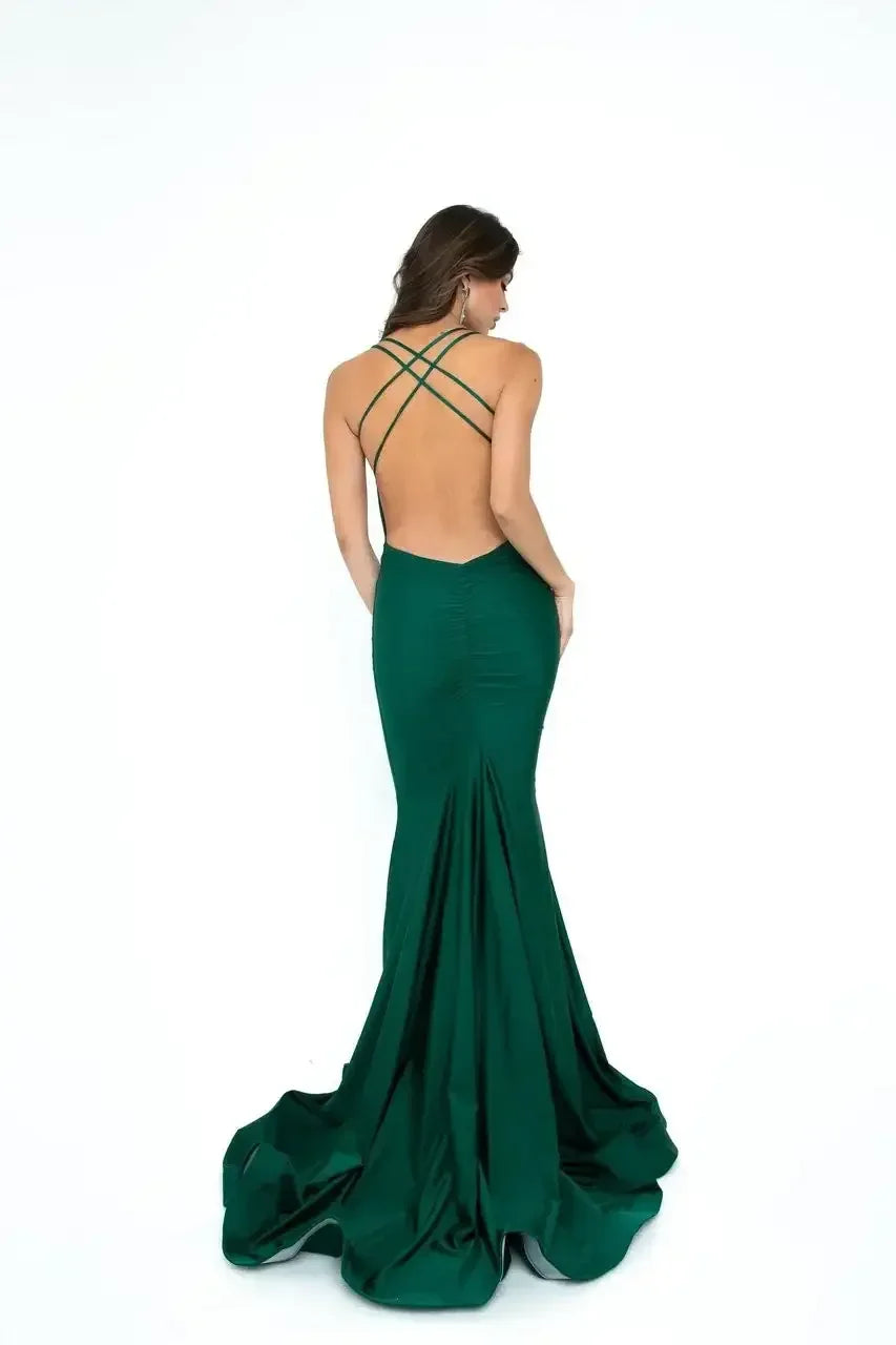 A woman in a fitted, deep green evening gown stands with her back facing the viewer. The dress features a low back and crossed straps, with a flowing skirt cascading down.