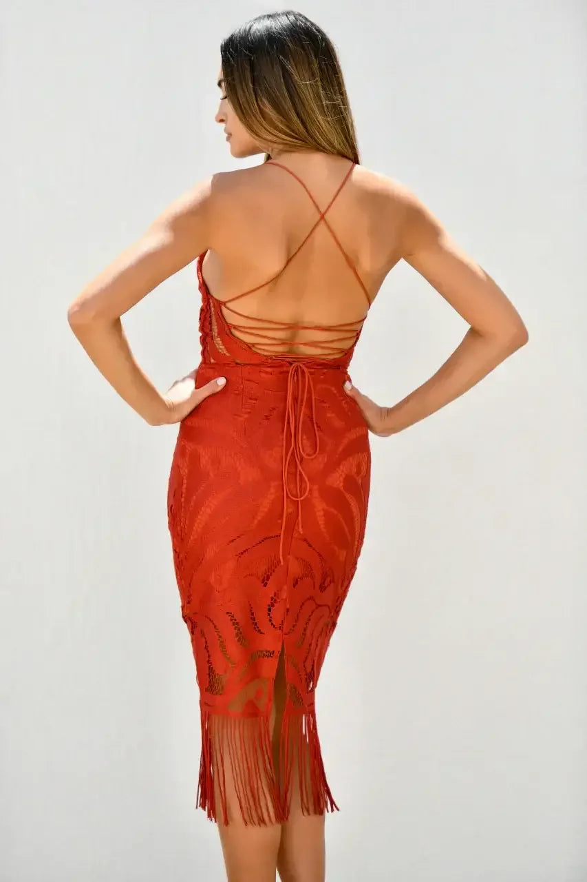 A woman is standing with her back to the viewer, wearing a fitted red dress with a backless design and fringed hem, against a plain white background.