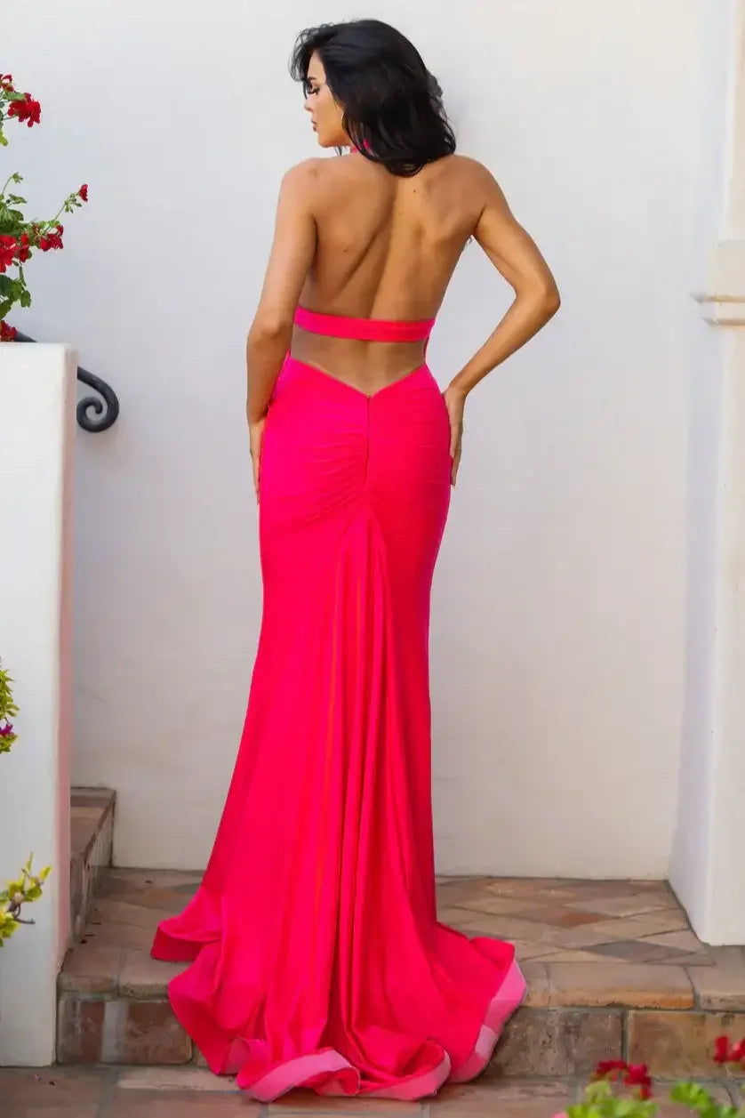 A woman in a vibrant pink gown stands with her back to the viewer, highlighting the dress's fitted design and open back. She is positioned outdoors near blooming flowers and a white wall.