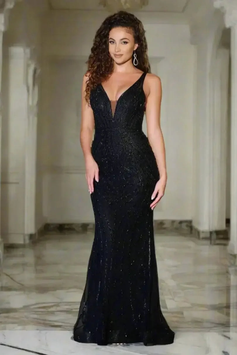 A woman stands confidently in a sparkly black evening gown, showcasing elegant curves. The urban night skyline glimmers behind her, creating a sophisticated and glamorous atmosphere.