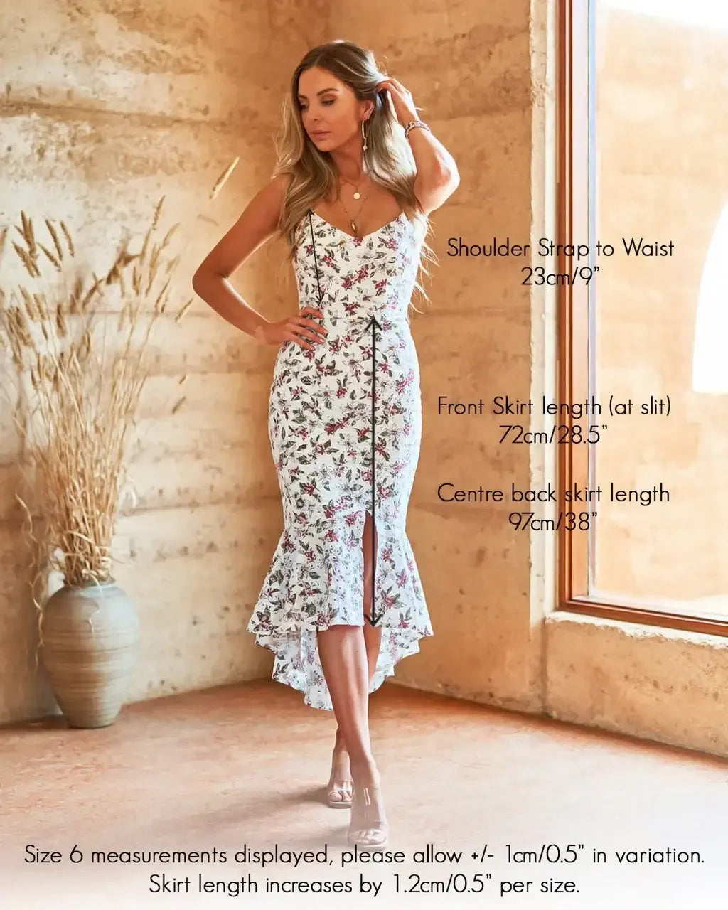 A woman in a floral dress stands gracefully, adjusting her hair. She is inside a textured, earthy-toned room with a large window and a plant nearby. Text details skirt measurements and variations.