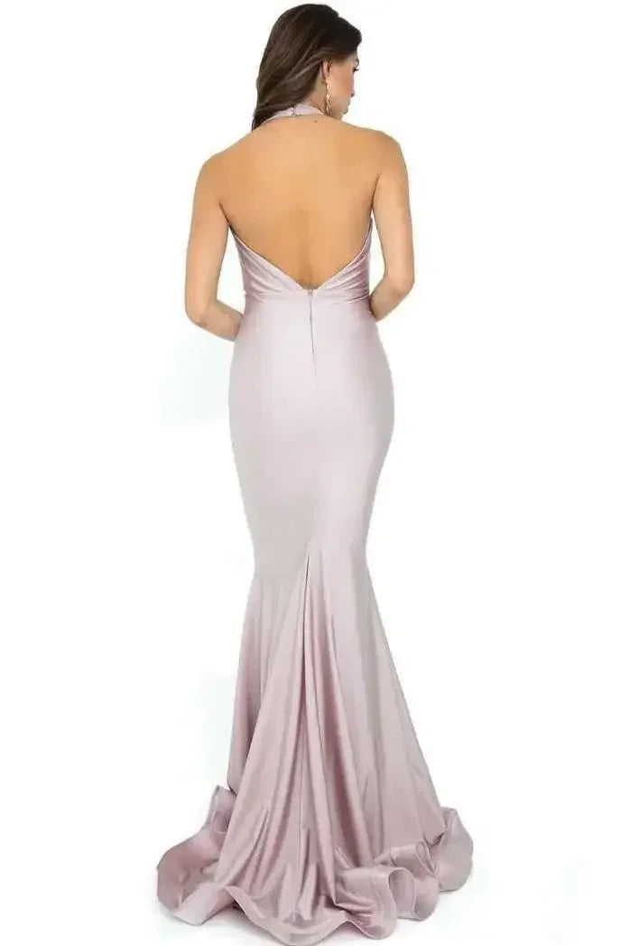 A woman stands wearing a fitted, light pink evening gown that flows elegantly to the floor. The dress has a low back and a flared hem, accentuating her silhouette.