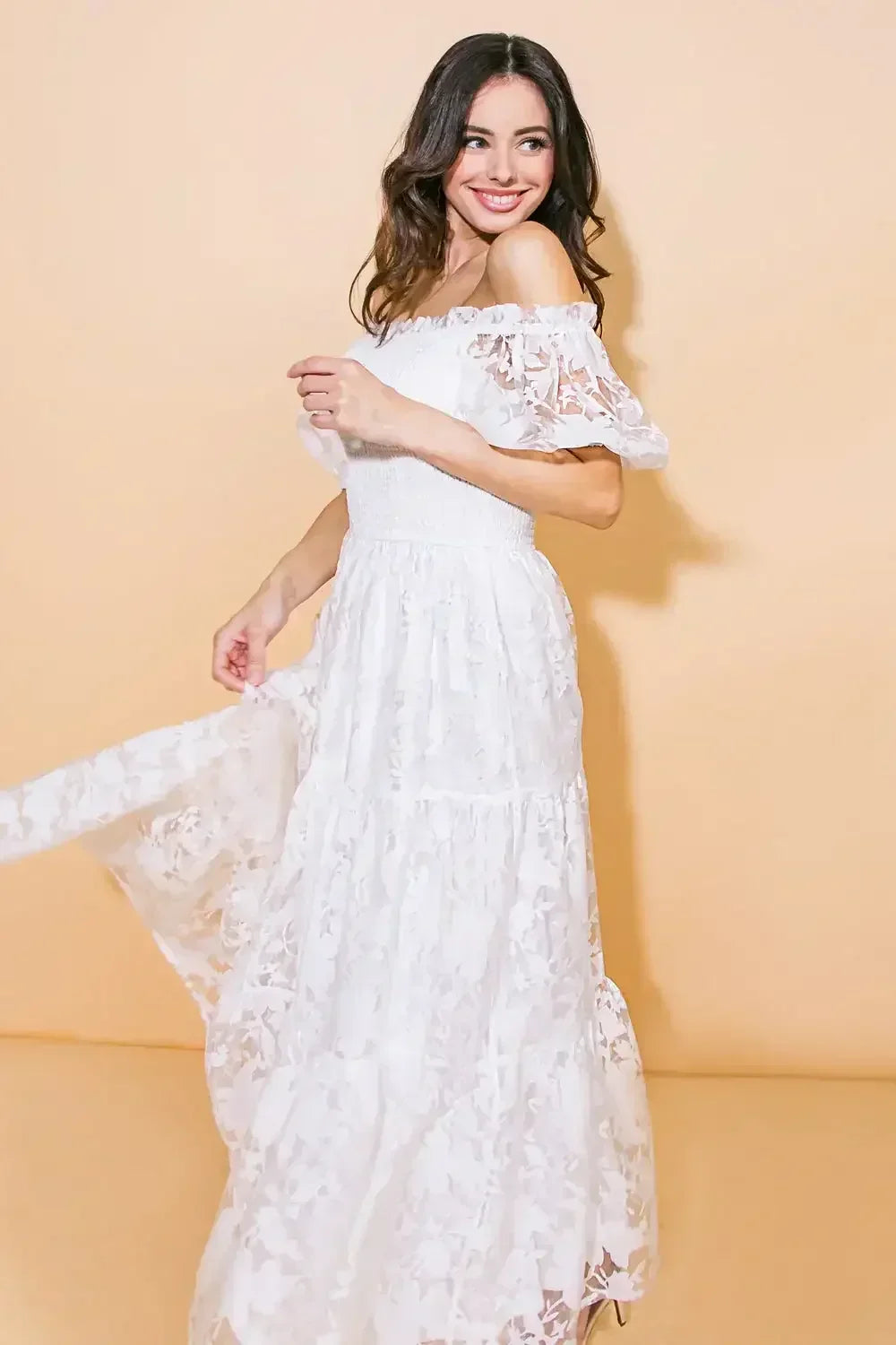 A woman in a white, floral lace dress spins joyfully, her hair flowing, against a soft, beige background, creating a vibrant and cheerful atmosphere.