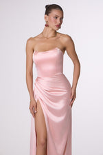 Woman wearing a pink strapless gown with a slit on a white background