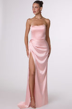 Woman wearing a strapless pink evening gown with a high slit on a white background