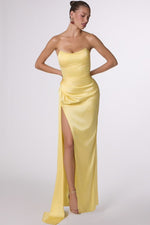 Woman wearing a yellow strapless gown with a high slit on a white background