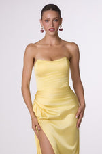 Woman wearing a yellow strapless dress with a slit on a white background
